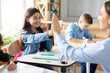 © Home-stock - Happy European girl giving high five to her teacher, sitting in classroom, woman helping female child student, giving support during lesson