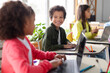 © Home-stock - Group of children sitting in school classroom with laptops on desk, talking with each other, studying. Classmates study in classroom. Back to school.