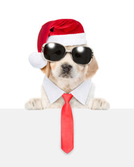 Canvas Print - Funny Golden retriever puppy wearing sunglasses, necktie and santa hat looks above empty white banner. isolated on white background