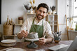 © sofiko14 - Workspace shows artistic creativity and craftsmanship, highlighting serene atmosphere of pottery studio. Male artist carefully shaping clay pot in rustic studio filled with pottery tools and materials