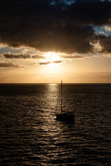 Wall Mural - a silhouetted sailboat at sunset on the ocean near the islands