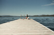 © Cavan Images - Child sitting on a dock overlooking a calm lake in the mountains