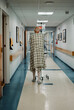 © Cavan Images - elderly male cancer patient wearing gown walks down hall in hospital