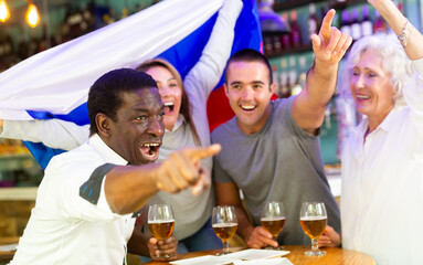 Wall Mural - Happy multiracial friends football fans holding the flag of Russia, enjoing game and beer in the bar