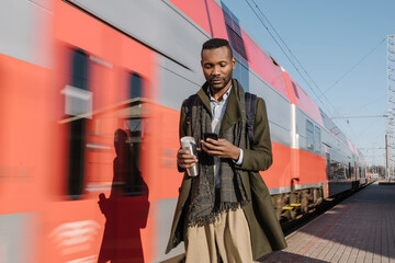 Wall Mural - Portrait of stylish man using smartphone next to a train