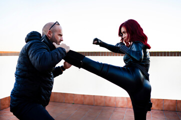 Redheaded woman wearing black leather catsuit fighting against man on rooftop