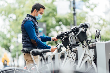 Wall Mural - Young man using smart phone at bicycle parking station during coronavirus