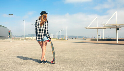 Wall Mural - Back view of young woman with longboard standing in front of beach promenade, partial view