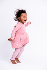 Portrait of barefoot little girl dressed in pink hopping in front of white background