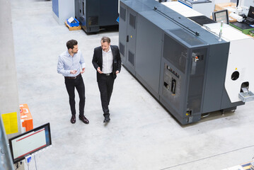 Wall Mural - Two businessman observing industrial robots in factory