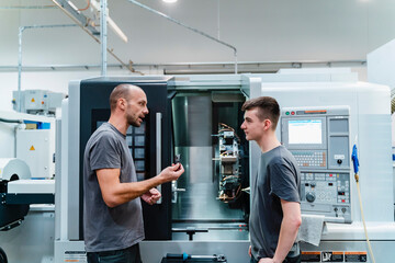 maintenance engineer giving instruction to coworker while standing against machinery at industry