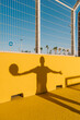 © tunedin - Shadow of young man holding basketball on yellow wall in sports court