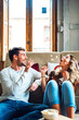 © tunedin - Cheerful young couple sitting at home and playing with popcorn