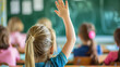 © 沈军 贡 - Close up of a child girl with blonde hair sitting in a classroom and raising her hand to ask the teacher a question during class at school