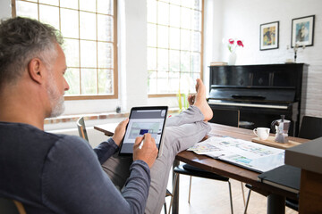 Poster - Mature man working from his home office with feet up, using tablet