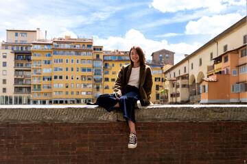 Wall Mural - Italy, Florence, smiling young woman resting on a wall in the city