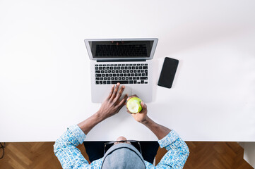 Wall Mural - Young man eating green apple while working at home office desk