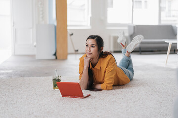 Poster - Young woman using laptop, lying on floor, thinking