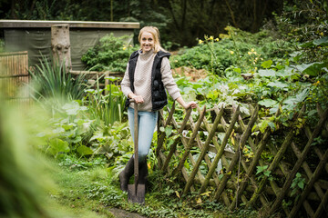 Portrait of smiling young woman with spade in garden