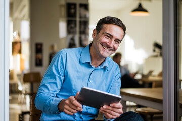 Poster - Smiling businessman with tablet sitting at open French door