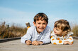 © tunedin - Portrait of boy and his little sister lying side by side on boardwalk having fun
