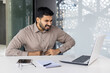 © Liubomir - Businessman in office attire experiencing stomach pain while working on a laptop at a modern office desk