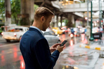 Canvas Print - Young businessman using smartphone in Bangkok during a rainy day