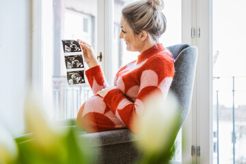 Wall Mural - Pregnant woman holding ultrasound image at home