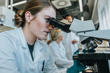 Assistant analyzing human brain microscope slide while sitting with scientist in background at laboratory