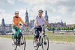 © tunedin - Smiling senior couple riding electric bicycle while exploring Hausmannsturm, Dresden, Germany