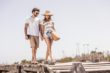 Poster - Young couple walking along a boardwalk from the beach