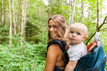 portrait of smiling mother hiking in the woods with baby boy in backpack