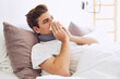 © tunedin - Sick young man blowing nose while lying on bed at home