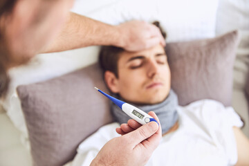 Close-up of doctor examining patient's temperature sleeping on bed at home