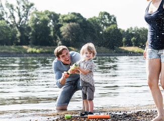 Wall Mural - Father and son having fun at the riverside, playing with a water gun