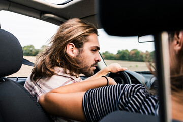 Poster - Young man looking at woman in a car