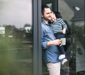 Father with cup of coffee carrying son at terrace door at home