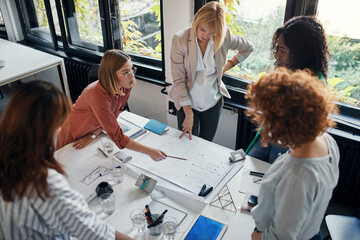 Canvas Print - Businesswomen having a meeting in office with blueprints on table