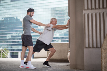 Wall Mural - Fitness instructor guiding senior man doing a stretching exercise