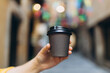 © mdyn - Woman gives paper black coffee cup or tea on urban background. Take away or delivery concept. Copy space. Place for your text on mug, mockup.