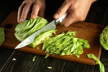 Wall Mural - Cutting cabbage with a knife on a cutting board to prepare a salad or vegetarian dish.