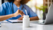 © Your Hand Please - pill bottle on white table with blurred doctor in background, symbolizing medical care and pharmaceutical treatment