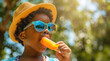 © Kien - boy wearing sunglasses and a hat licking a popsicle, summer fun activity in the park, outdoors. A little kid eating an ice cream bar on a hot day