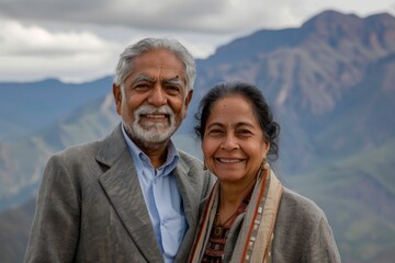 Sticker - Portrait of a smiling indian couple in their 70s dressed in a stylish blazer in front of backdrop of mountain peaks