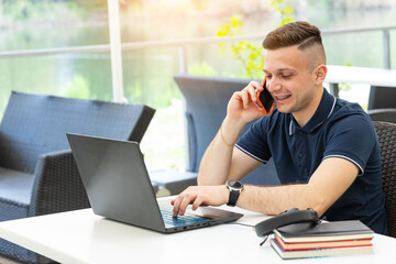 Young male entrepreneur talking on the phone and working with a laptop on the table. Work as a freelancer.