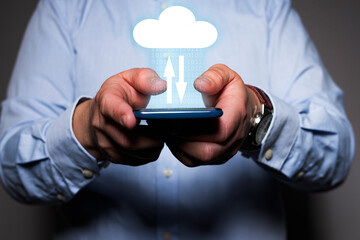 Close-up of a unrecognizable man's hands holding a mobile phone with a icon of a cloud over it and two arrows symbolizing data transfer