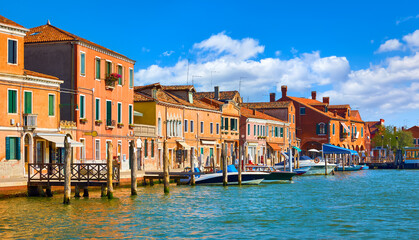 Wall Mural - Murano Island in Venice, Italy. Antique italian houses on the channel with motorboats. Blue sky and white clouds murano. Sunny summer day. Popular touristic travel destination Europe