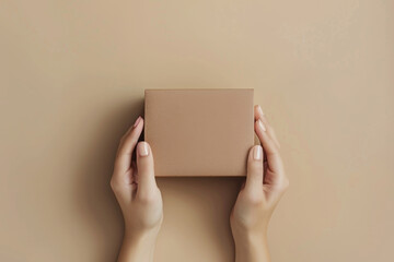 Wall Mural - Woman hands holding brown ecological package box made of natural corrugated cardboard. Mockup parcel box on ivory background. Top view. Packaging, shopping, delivery concept