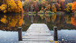 © Saeed - A tranquil lake mirrors the vibrant fall foliage of surrounding trees, with a wooden dock stretching into the serene autumn air.