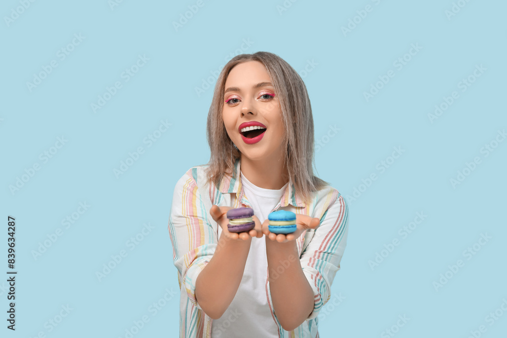Happy young woman with different sweet macaroons on blue background